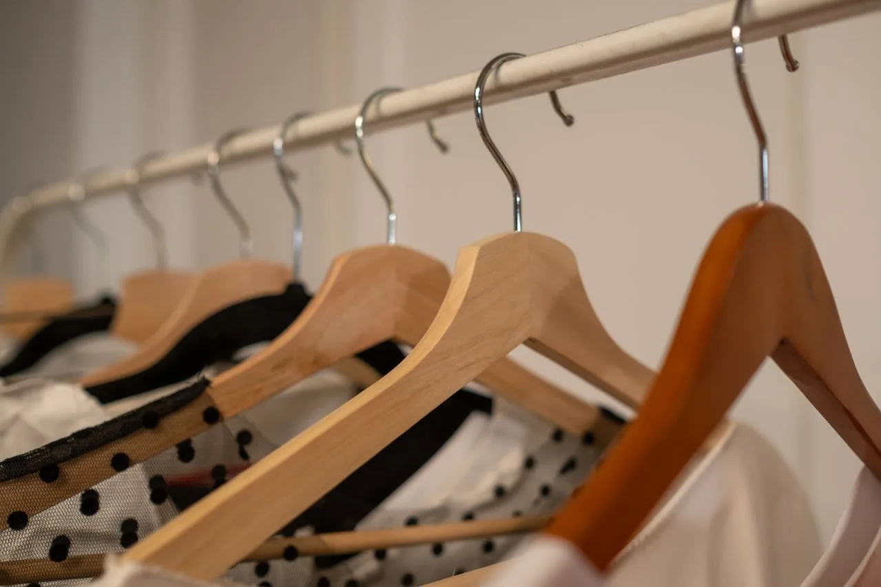Roupas organizadas em cabides de madeira em uma arara.
