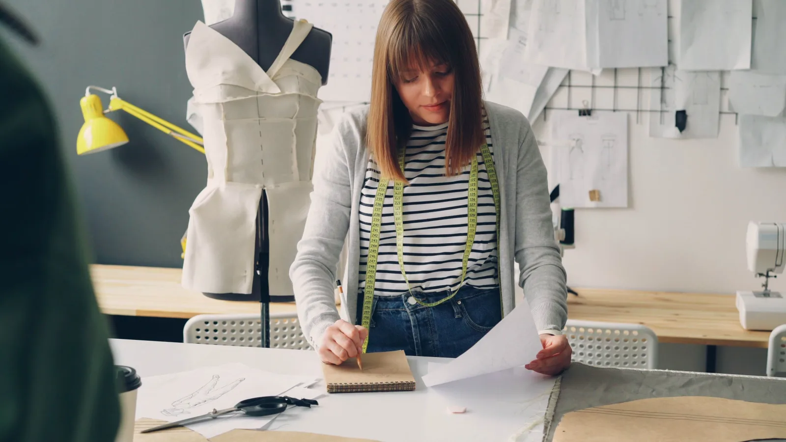 Profissional de moda trabalhando com croquis e tecidos em um ateliê de criação.