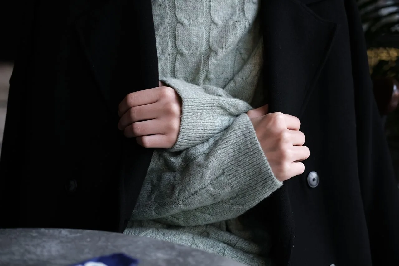 Pessoa usando tricô cinza sob casaco preto em um look de inverno em camadas.