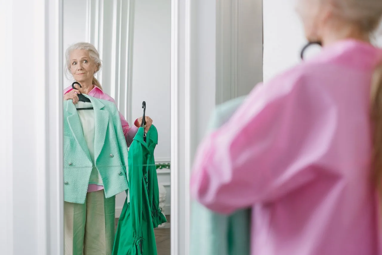 Mulher comparando duas peças de roupa diante do espelho.