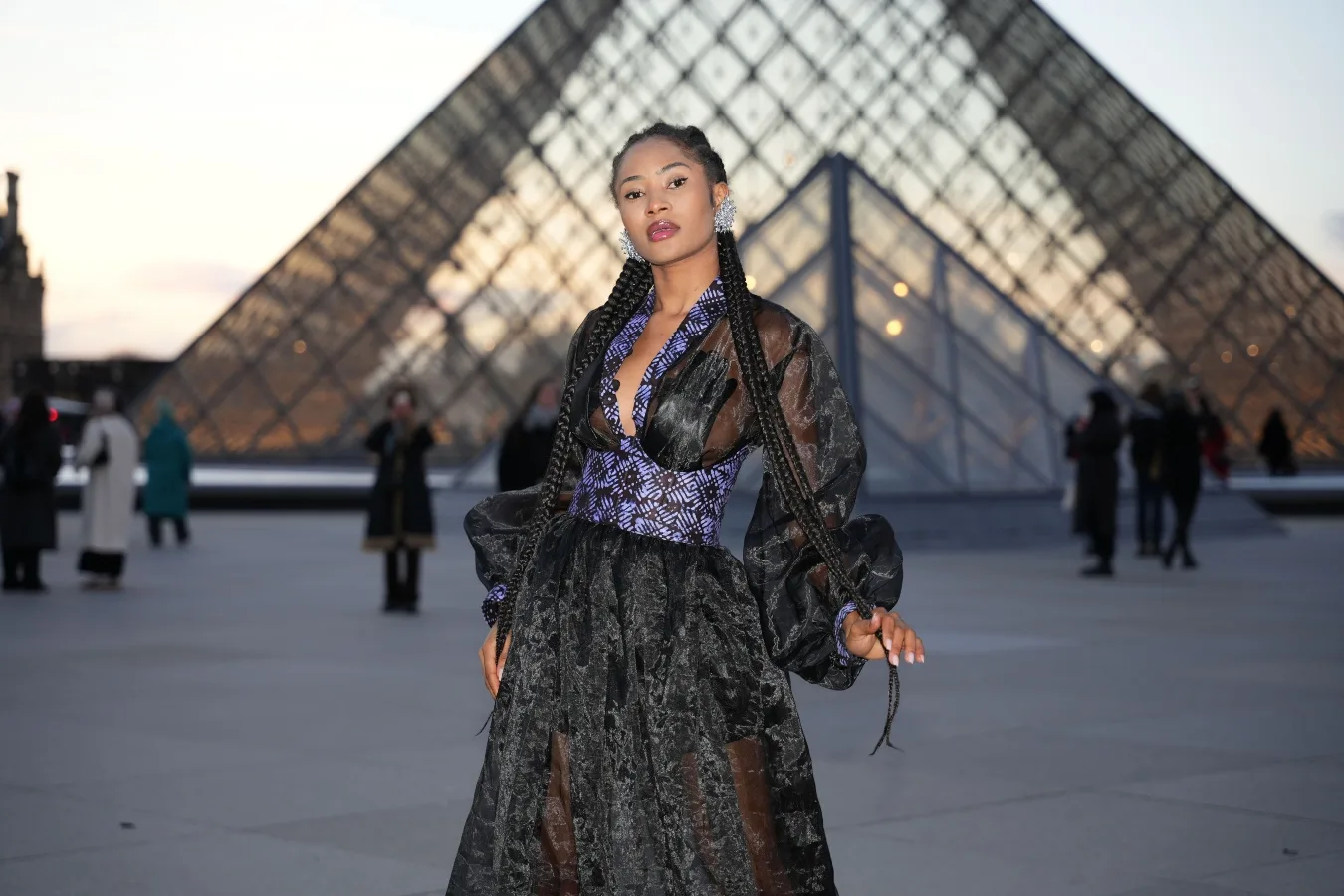 Mulher com look transparente e texturizado diante da Pirâmide do Louvre em Paris