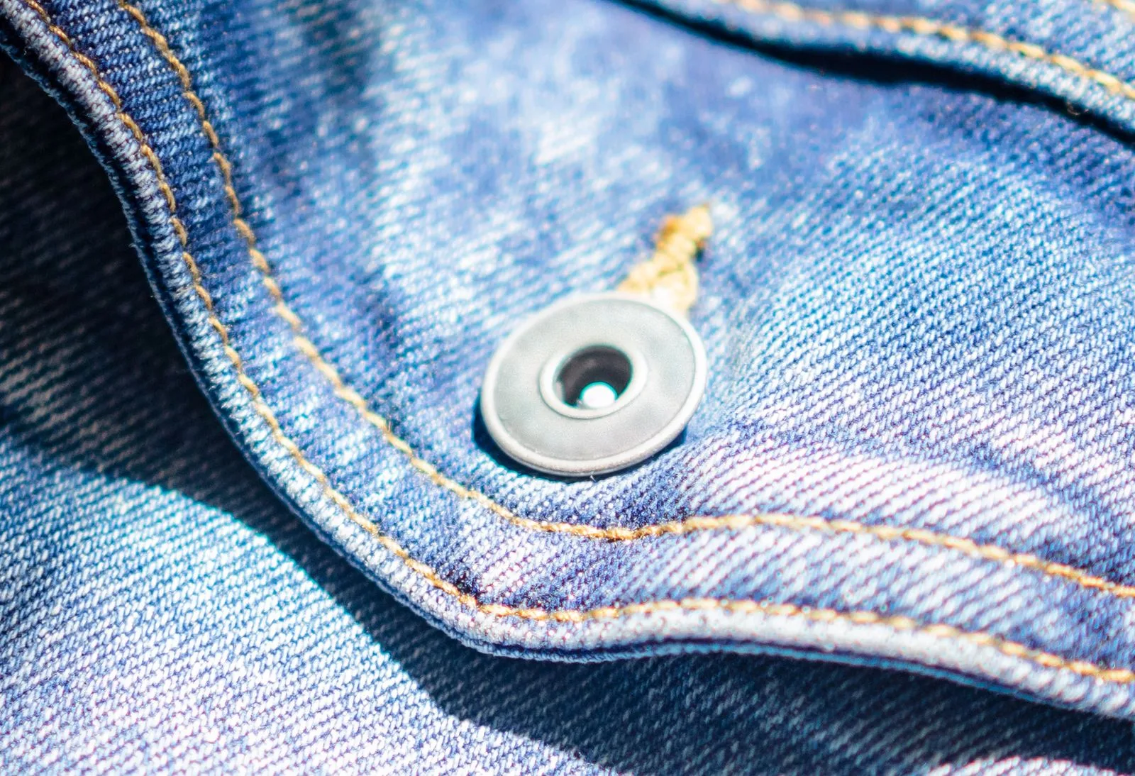 Close em tecido jeans com costura aparente, acabamento e detalhe metálico.