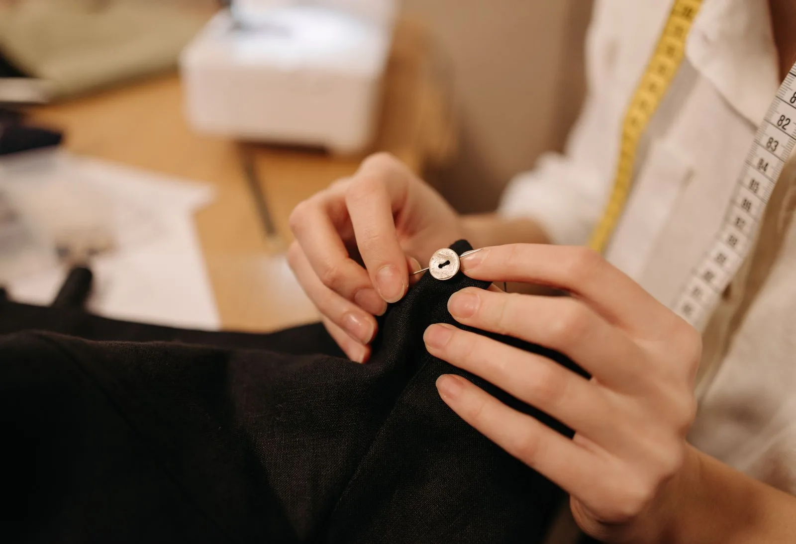 Pessoa realizando um pequeno ajuste em uma peça de roupa escura, com fita métrica sobre o ombro.