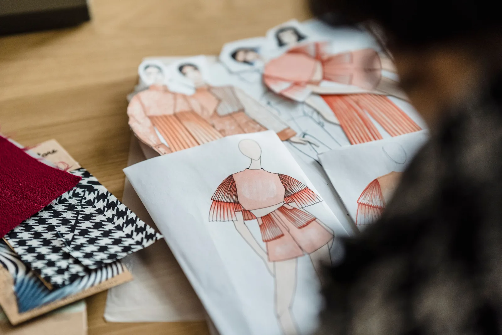 Croquis de moda e amostras de tecidos sobre uma mesa durante o desenvolvimento de uma coleção.